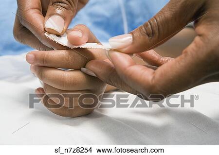 Picture - Close up of African nurse putting adhesive bandage on child’s thumb. Fotosearch