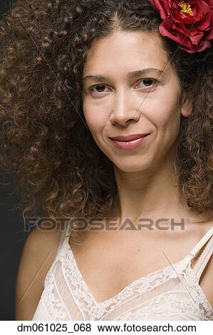 Stock Photo - Close up of Hispanic woman smiling with flower in hair. Fotosearch