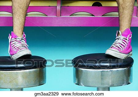Stock Photo - Close up of man’s feet in pink sneakers on stools. Fotosearch