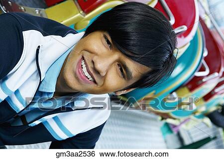 Stock Photograph - Close up of young Hispanic man smiling next to carnival ride. Fotosearch
