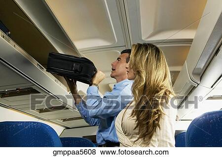 Couple stowing luggage in overhead compartment on airplane View Large Photo Image Stock Photo - Couple stowing luggage in overhead compartment on airplane. Fotosearch