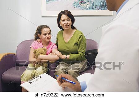Stock Image - Doctor talking to Hispanic mother and daughter in waiting room. Fotosearch