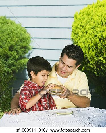 Hispanic father helping young son eat hamburger View Large Photo Image Stock Photo - Hispanic father helping young son eat hamburger. Fotosearch