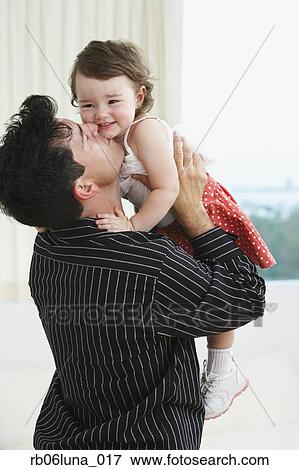 Stock Photo - Hispanic father holding up and kissing young daughter. Fotosearch