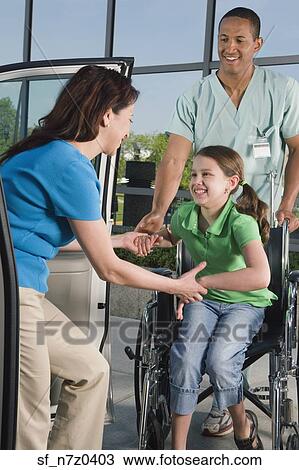 Stock Image - Hispanic girl in wheelchair leaving hospital with mother. Fotosearch