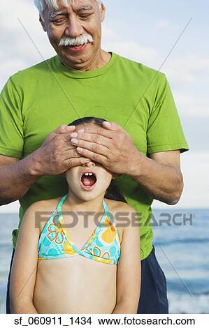 Hispanic grandfather covering granddaughter’s eyes View Large Photo Image Picture - Hispanic grandfather covering granddaughter’s eyes. Fotosearch
