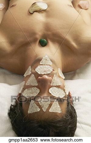 Stock Image - Hispanic man receiving stone and crystal spa treatment. Fotosearch