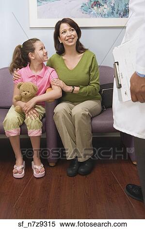 Stock Photography - Hispanic mother and daughter talking to doctor in waiting room. Fotosearch