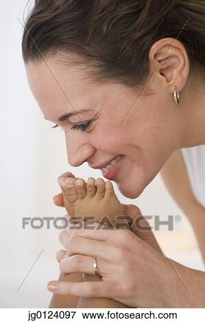 Stock Photo - Hispanic mother kissing baby’s feet. Fotosearch