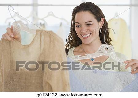 Stock Image - Hispanic woman comparing blouses. Fotosearch
