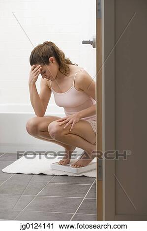 Stock Image - Hispanic woman frowning on bathroom scale. Fotosearch