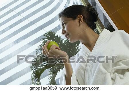 Stock Photo - Hispanic woman in spa bathrobe holding apple. Fotosearch
