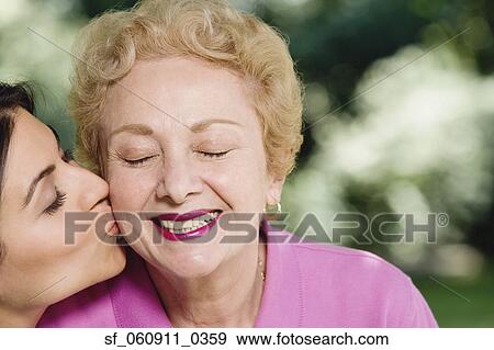 Stock Photo - Hispanic woman kissing mother on cheek outdoors. Fotosearch