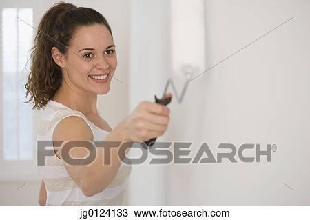 Stock Image - Hispanic woman painting wall with roller. Fotosearch
