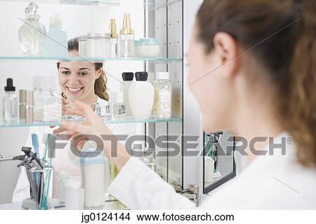 Picture - Hispanic woman reaching into medicine cabinet. Fotosearch