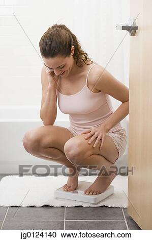 Stock Image - Hispanic woman standing on bathroom scale. Fotosearch