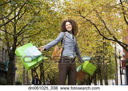 Stock Photo - Hispanic woman swinging shopping bags in urban park. Fotosearch