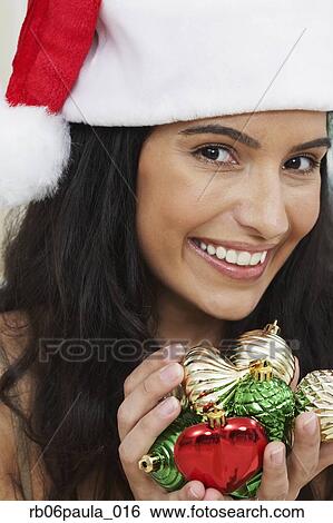 Stock Photograph - Hispanic woman wearing Santa hat and holding Christmas ornaments. Fotosearch