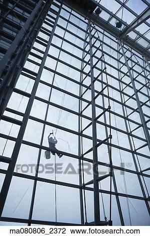 Stock Image - Low angle view of window washer hanging outside building. Fotosearch