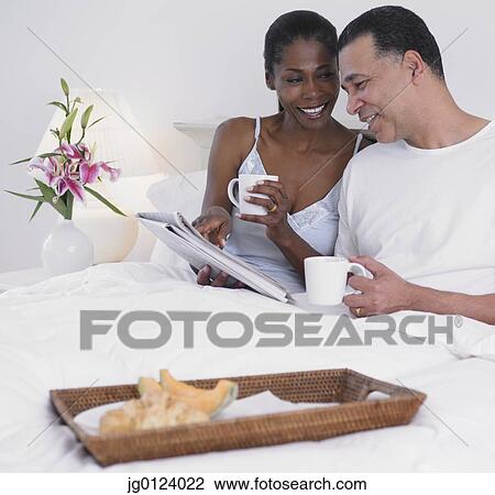 Stock Image - Middle-aged African couple having breakfast in bed. Fotosearch
