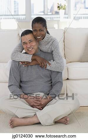 Stock Image - Middle-aged African couple hugging on sofa . Fotosearch