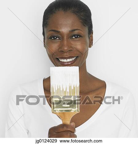 Stock Photo - Middle-aged African woman holding up paint brush. Fotosearch