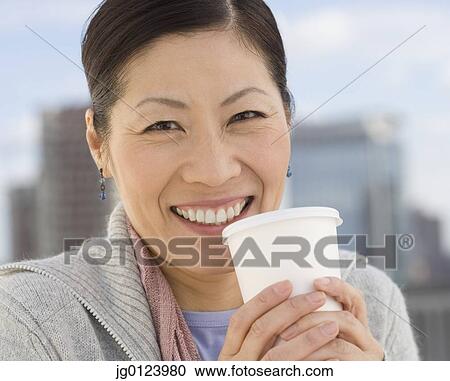 Stock Image - Middle-aged Asian woman holding coffee cup outdoors. Fotosearch