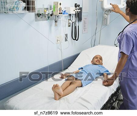 Stock Photo - Nurse checking on African boy in hospital bed. Fotosearch
