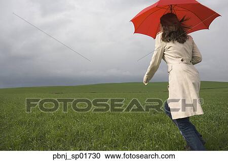 Rear view of woman running with umbrella in field View Large Photo Image Stock Image - Rear view of woman running with umbrella in field. Fotosearch