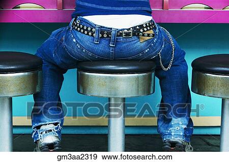 Rear view of young person with studded belt sitting on stool at counter View Large Photo Image Stock Photo - Rear view of young person with studded belt sitting on stool at counter. Fotosearch