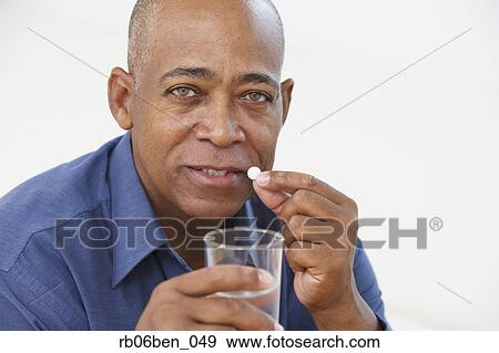 Senior African man taking medication with glass of water View Large Photo Image Stock Photo - Senior African man taking medication with glass of water. Fotosearch
