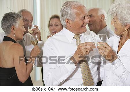 Senior couple toasting at party with friends in background View Large Photo Image Stock Photo - Senior couple toasting at party with friends in background. Fotosearch