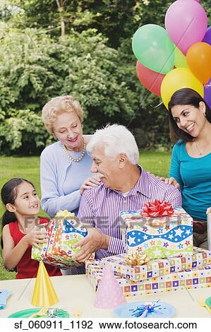 Stock Image - Senior Hispanic man receiving gifts at birthday party. Fotosearch