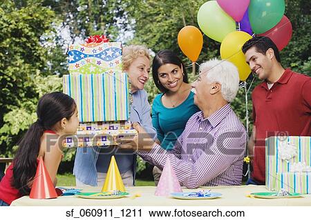 Stock Image - Senior Hispanic man receiving gifts at birthday party. Fotosearch