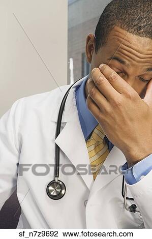 Stock Image - Tired African male doctor rubbing eyes. Fotosearch