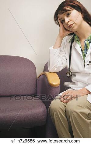 Stock Photograph - Tired Hispanic female doctor sitting with head in hand. Fotosearch