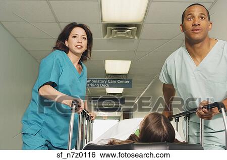 Stock Photograph - Two nurses wheeling gurney with patient in corridor of hospital. Fotosearch