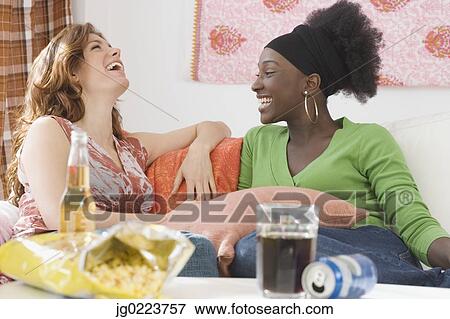 Stock Photo - Two women laughing on sofa. Fotosearch