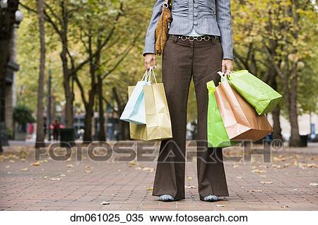 Woman holding shopping bags in urban park View Large Photo Image Stock Photography - Woman holding shopping bags in urban park. Fotosearch