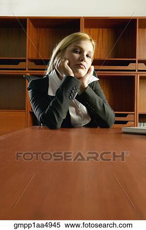 Stock Photography - Young Hispanic businesswoman sitting at conference table leaning chin in hands. Fotosearch