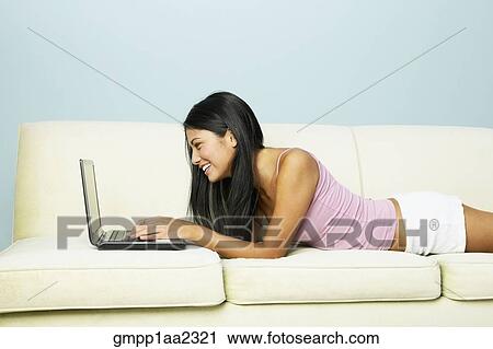 Stock Image - Young Hispanic woman using laptop on sofa. Fotosearch