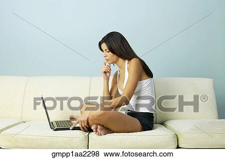 Stock Photo - Young Hispanic woman using laptop on sofa. Fotosearch