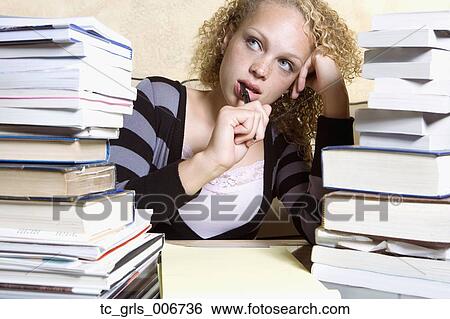 Stock Photograph - Young woman studying at desk with large stacks of books and notepad. Fotosearch