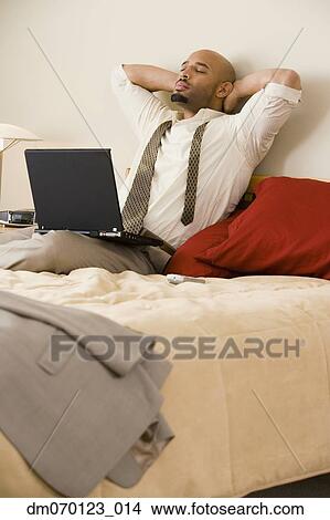 African businessman relaxing on bed with laptop View Large Photo Image Picture - African businessman relaxing on bed with laptop. Fotosearch