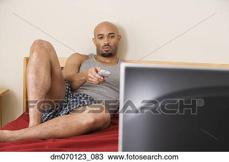 Stock Image - African man watching television in bed. Fotosearch