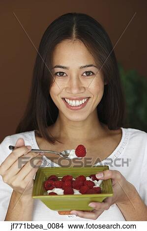 Picture - Asian woman eating fruit and cream. Fotosearch