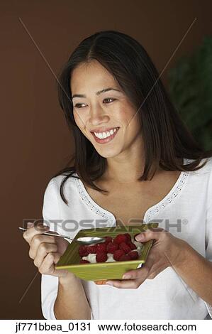Stock Image - Asian woman eating fruit and cream. Fotosearch