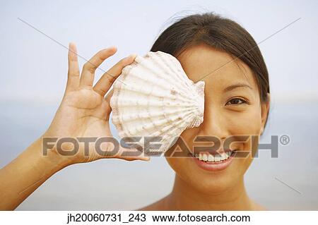 Asian woman holding seashell over eye View Large Photo Image Stock Image - Asian woman holding seashell over eye. Fotosearch
