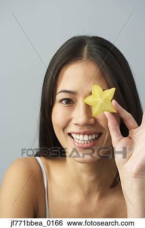 Stock Photograph - Asian woman holding star fruit over eye. Fotosearch