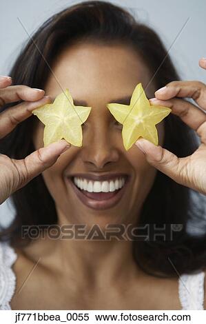 Stock Photography - Asian woman holding star fruits over eyes. Fotosearch